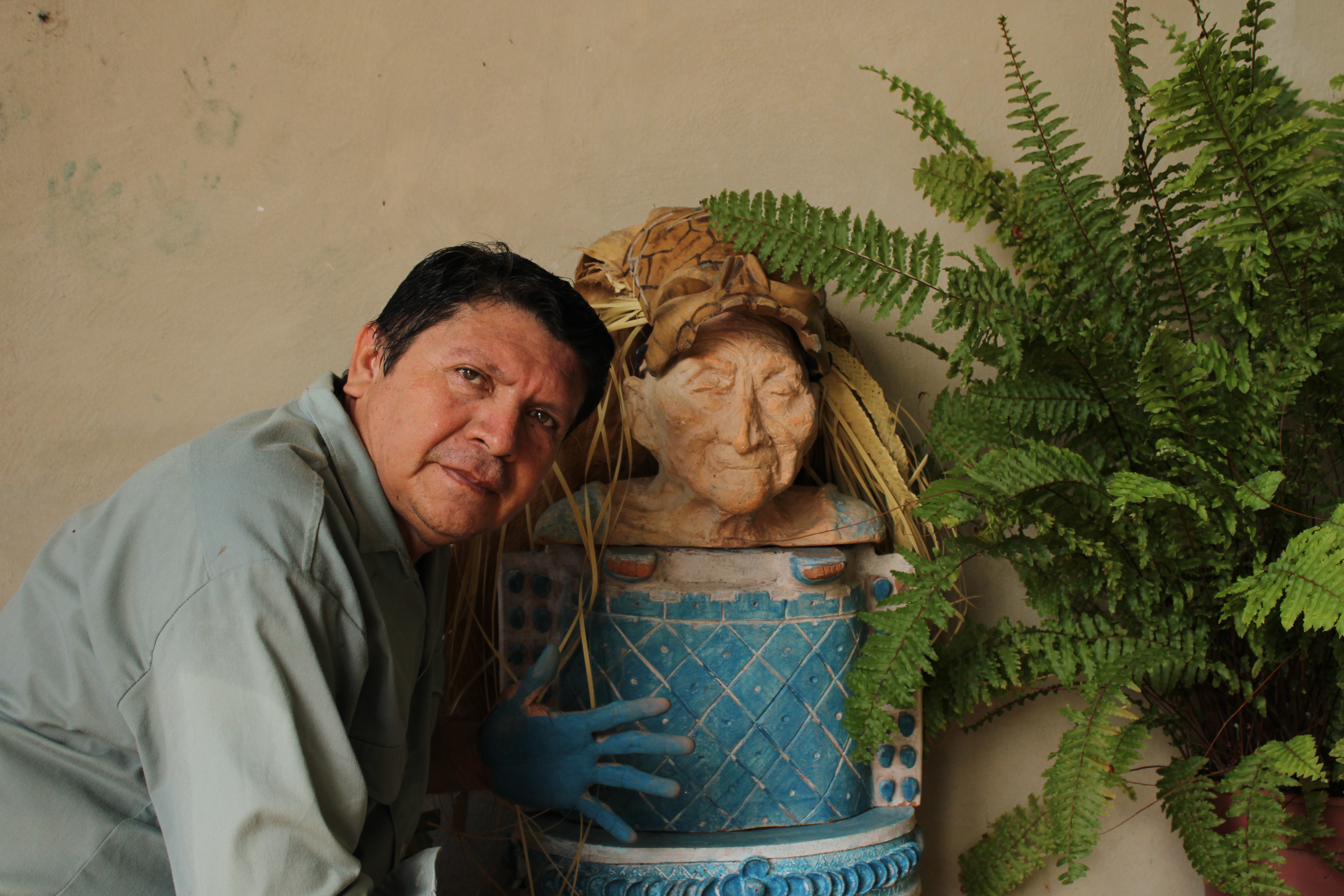 Luis May Ku, 49, poses next to a clay sculptor of an elderly woman from his community of Dzan, wearing a wooden mask adorned with dried palm leaves and painted in Maya Blue taken on 9 September,