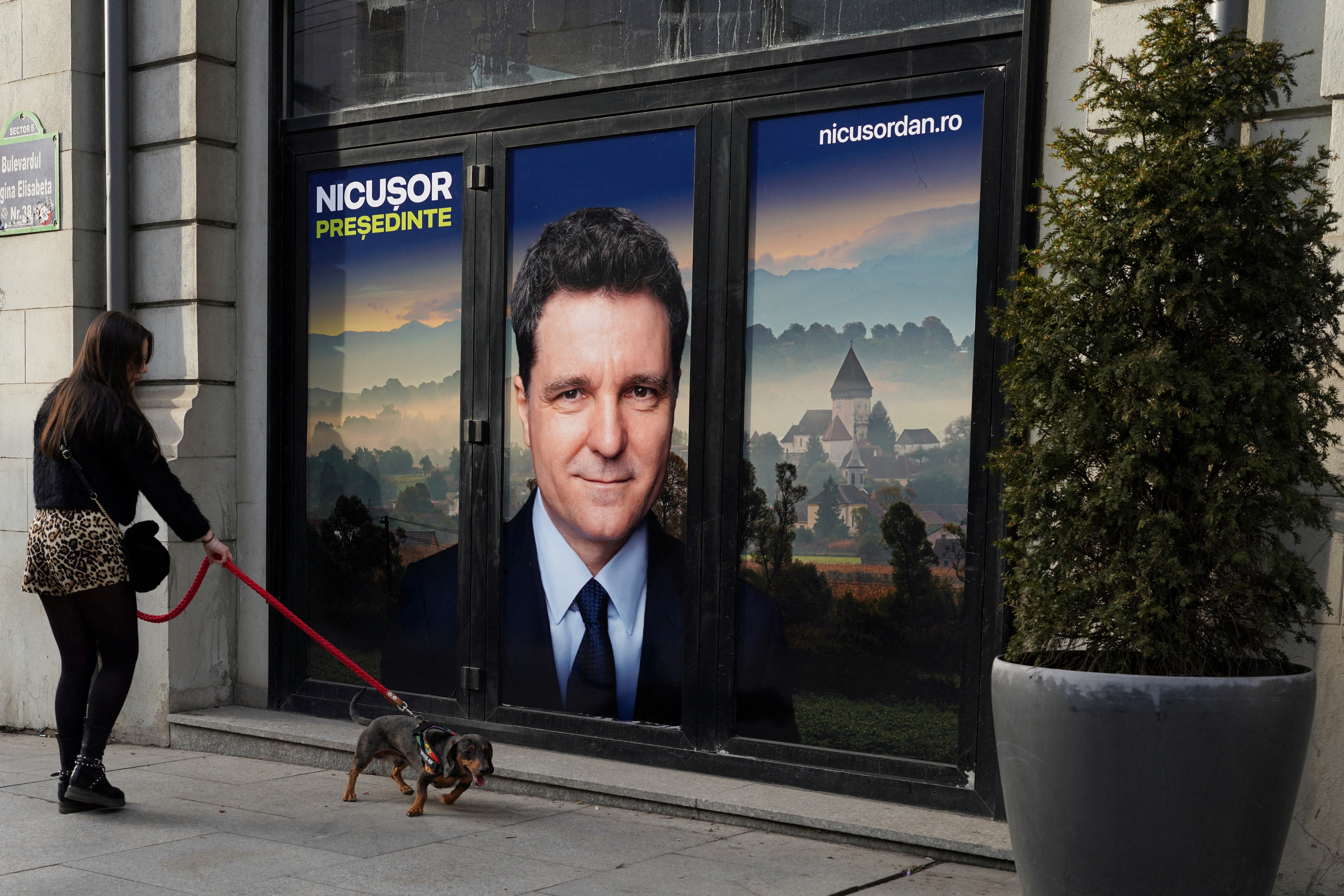 FILE PHOTO: A woman walks a dog past a poster of independent presidential candidate Nicusor Dan