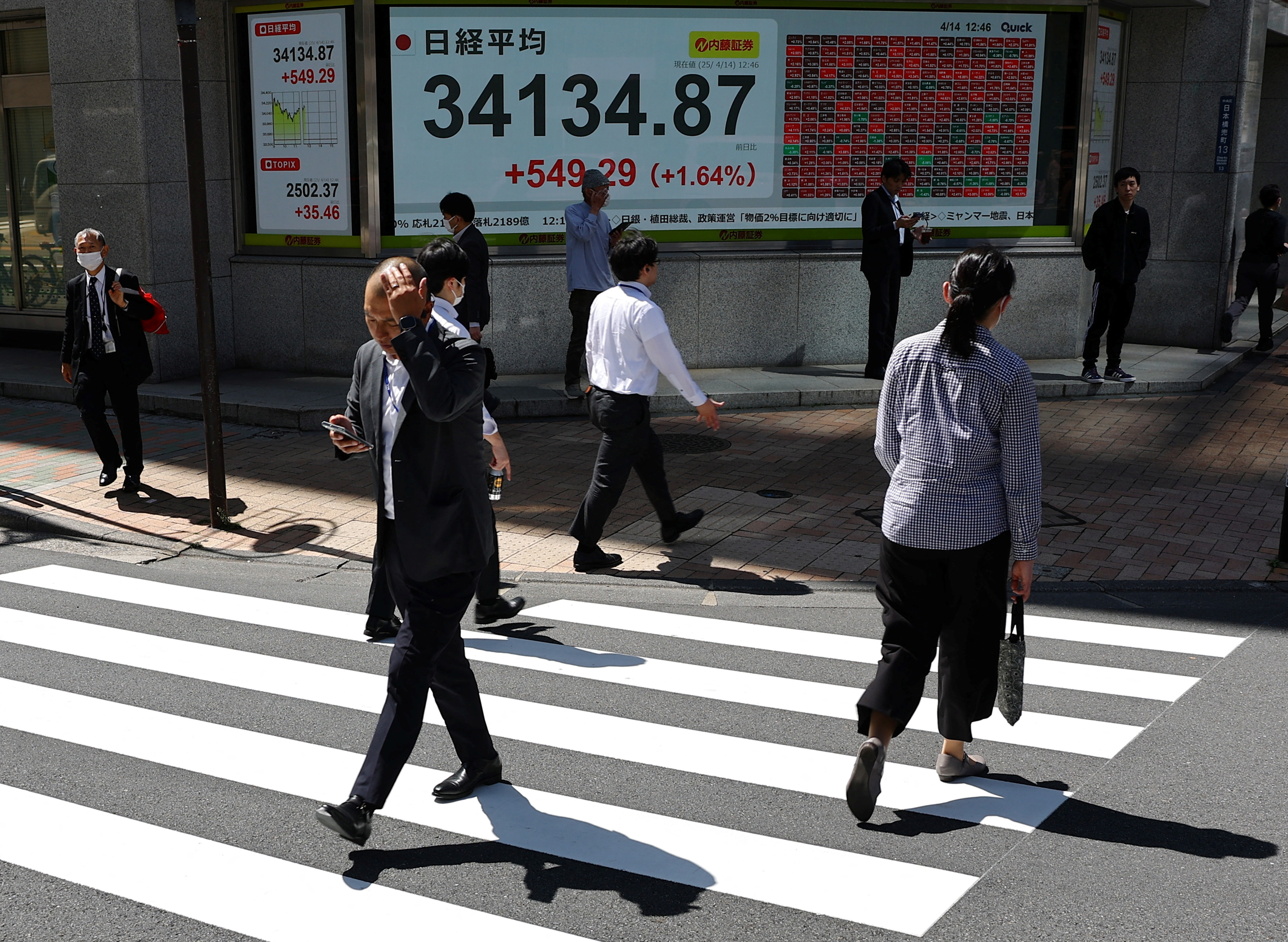 Pedestrians walk past a stock quotation board showing Nikkei share average outside a brokerage in Tokyo
