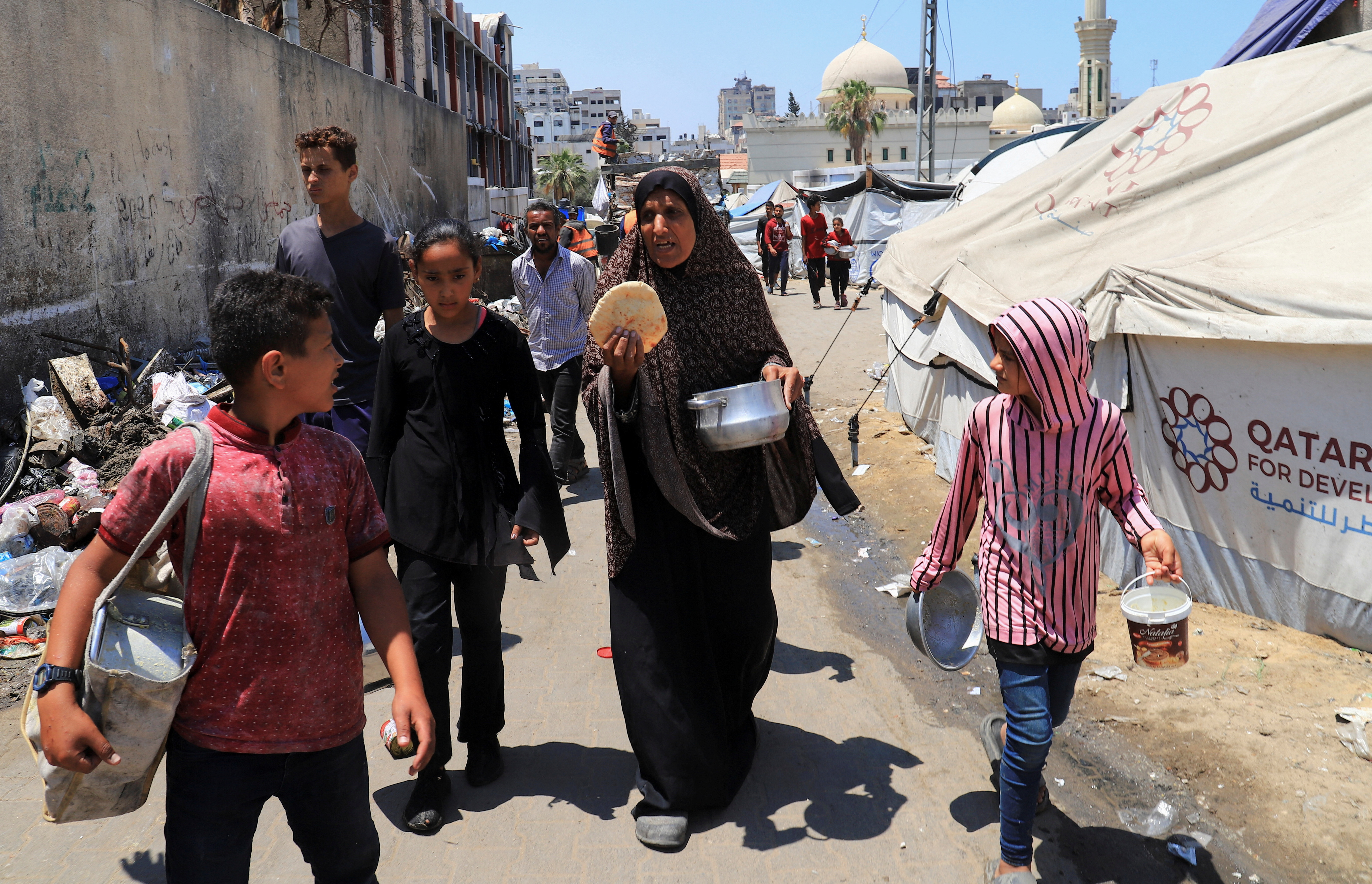Raseljena Palestinka Zeinab Abed hoda s djecom nakon što se vratila u svoj šator bez hrane iz dobrotvorne kuhinje u Gazi
