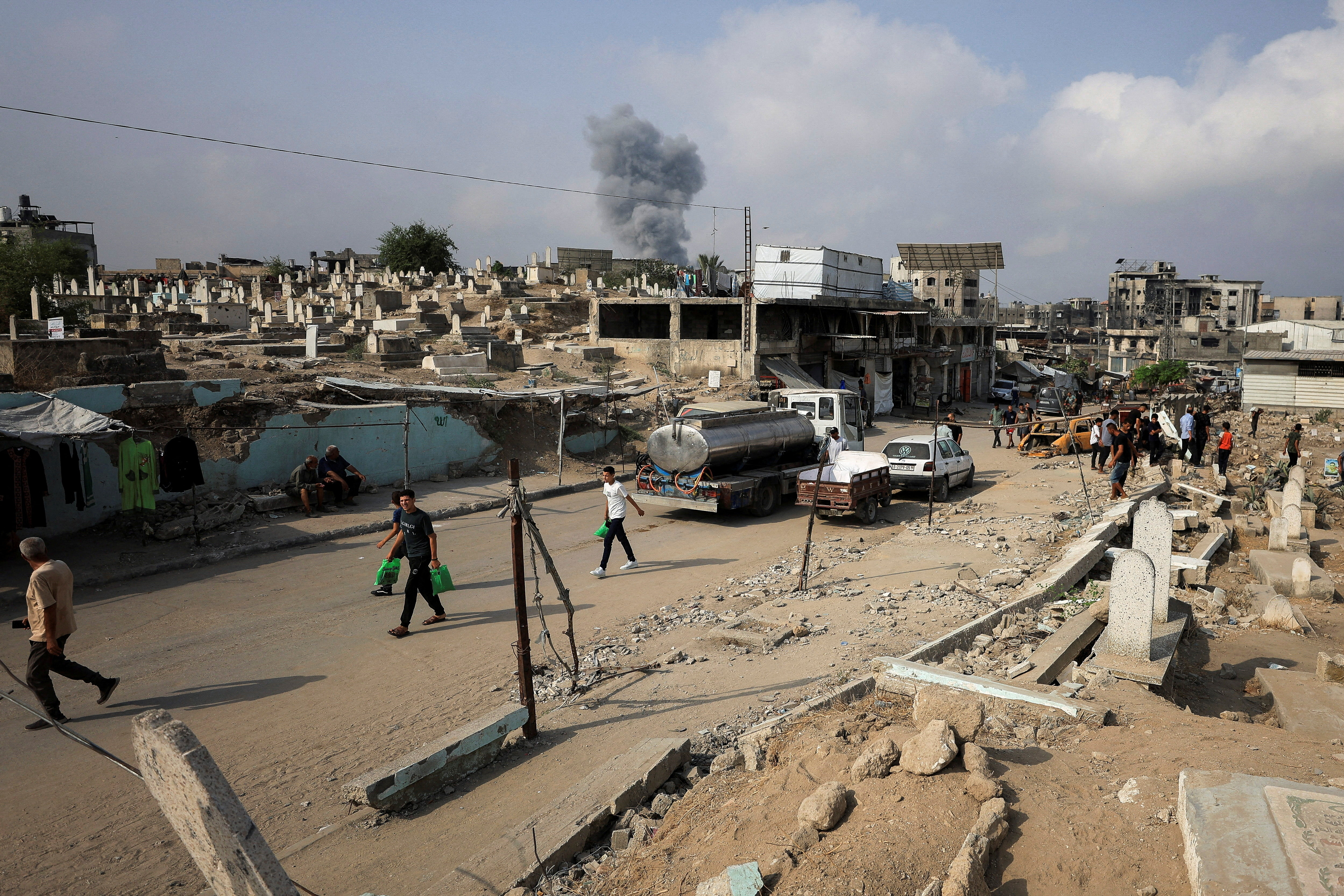 Palestinians walk past damaged graves as smoke rises following an Israeli strike, in Gaza City, August 13, 2025. REUTERS/Dawoud Abu Alkas   REFILE - QUALITY REPEAT     TPX IMAGES OF THE DAY