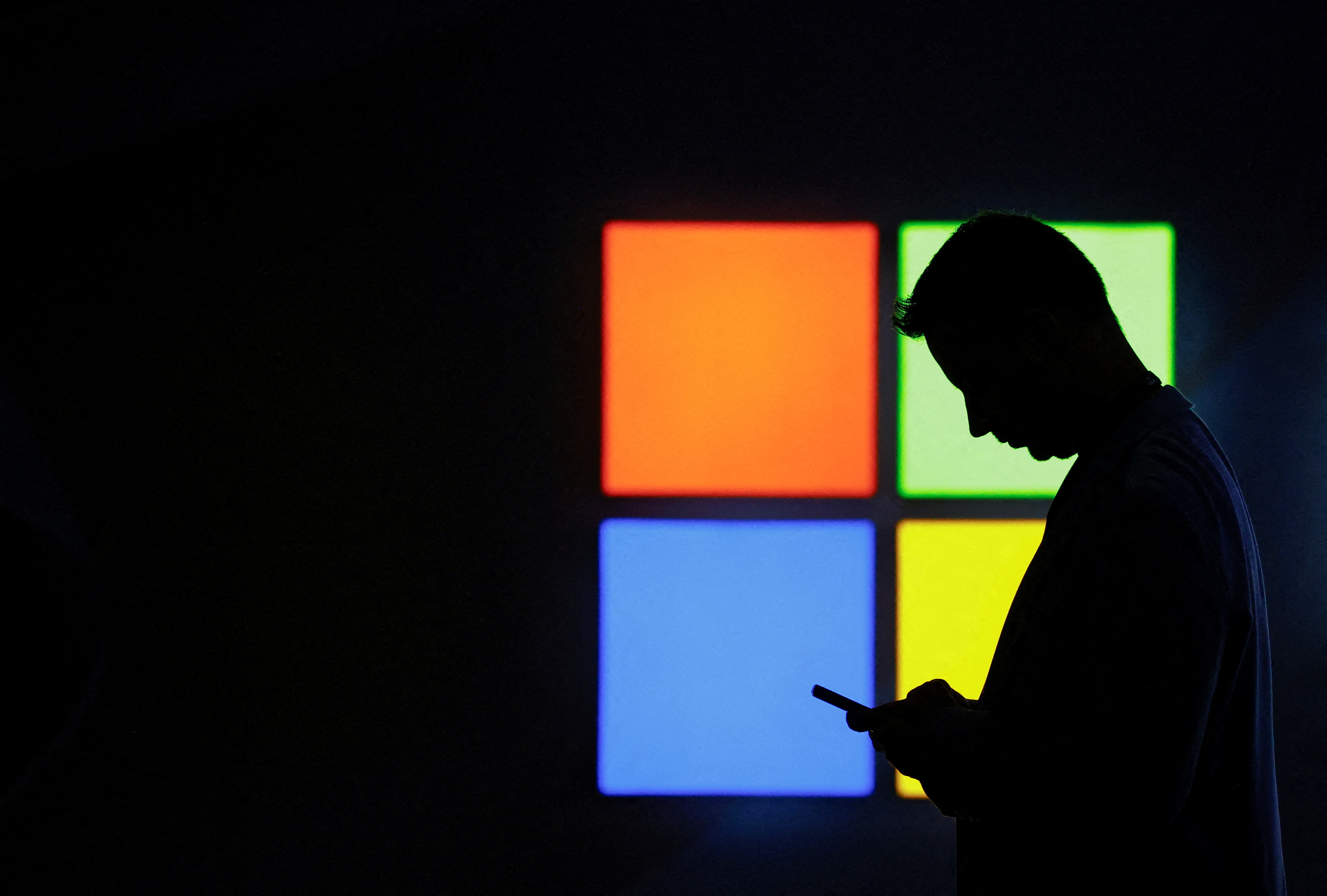 FILE PHOTO: A man looks at his phone as he passes by the Microsoft stand at the