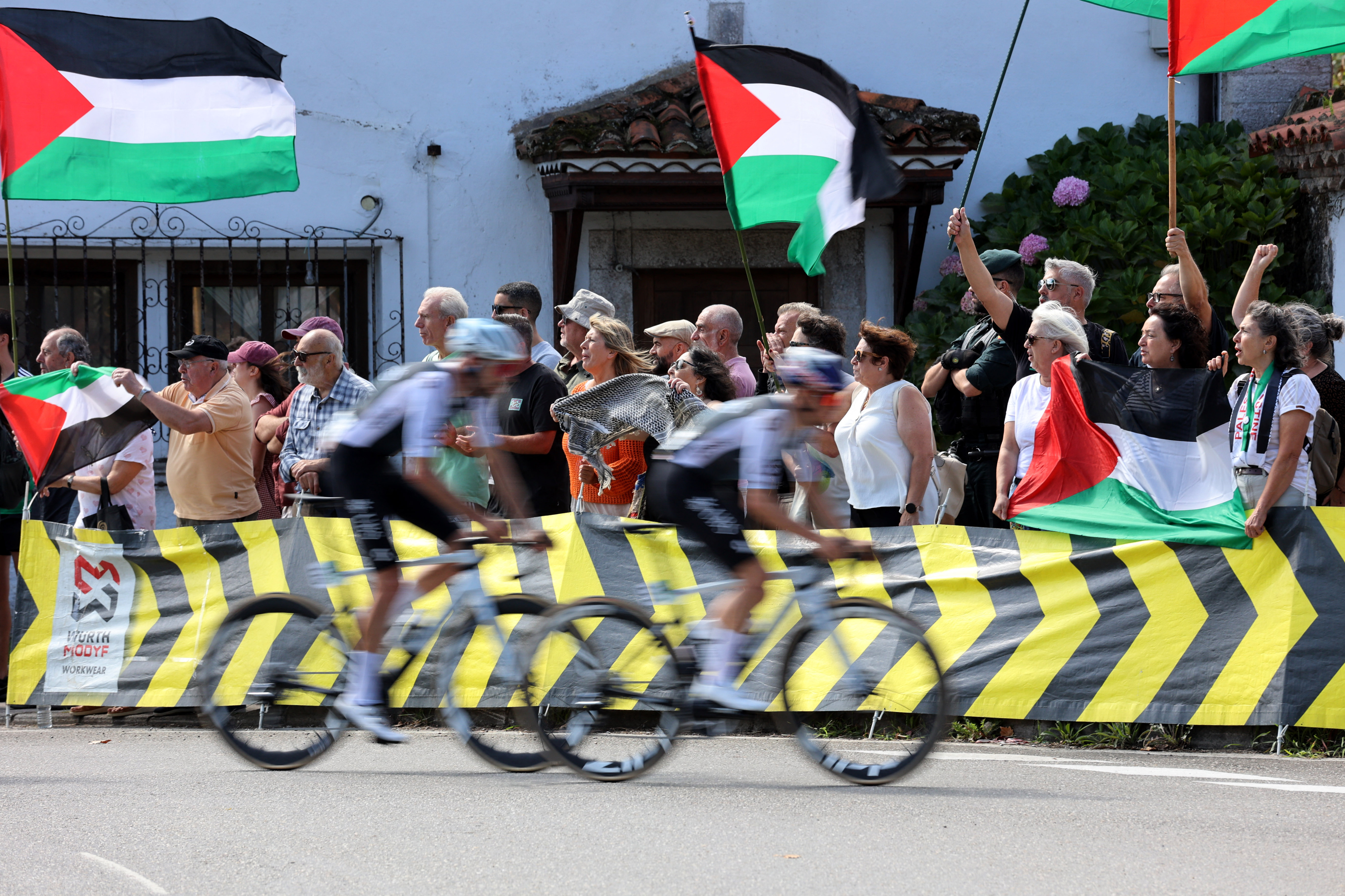 Cycling - Vuelta a Espana - Stage 13 - Cabezon de la Sal to L'angliru - Cantabria, Spain - September 5, 2025  Riders pass protesters with Palestine flags during stage 13 REUTERS/Pankra Nieto