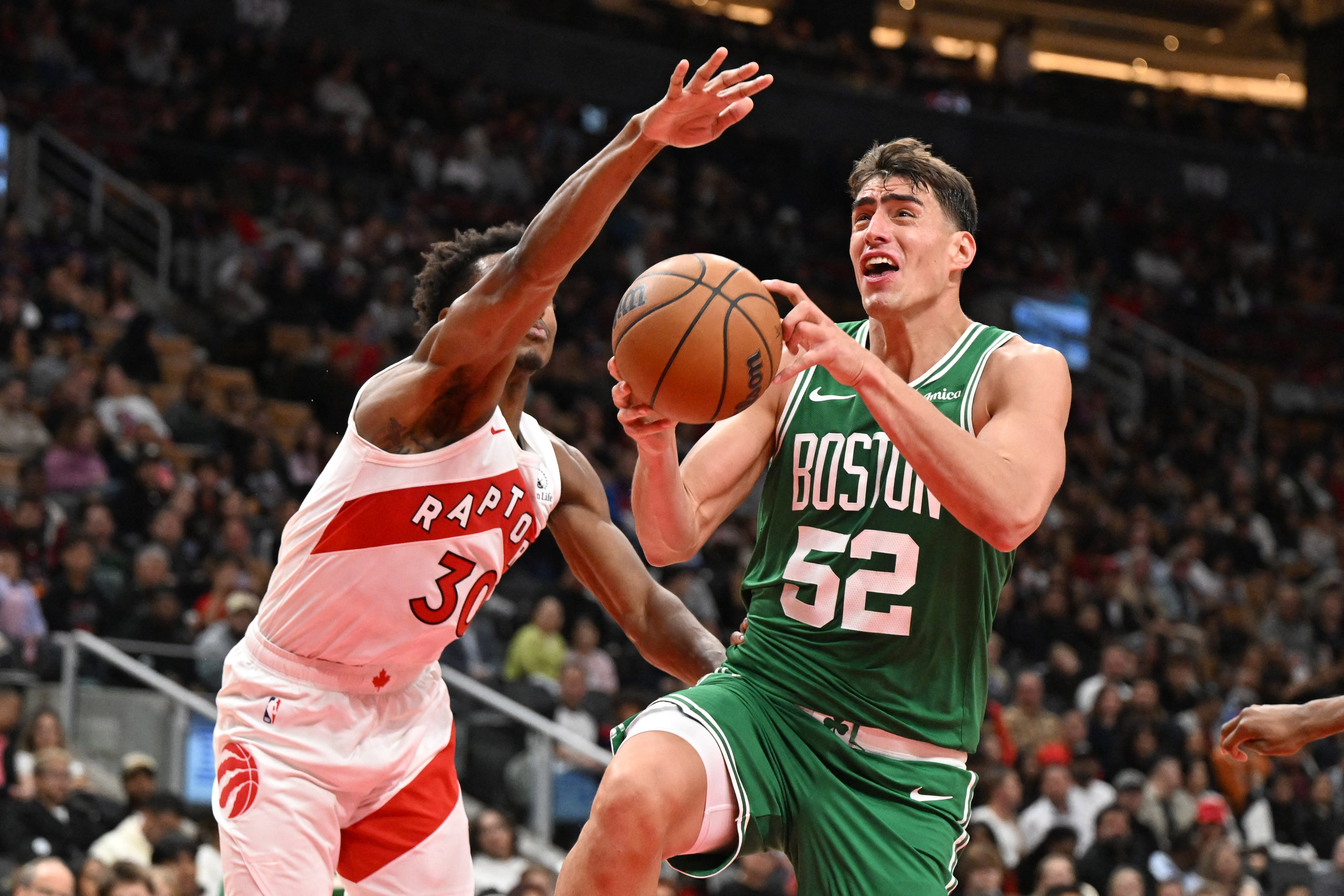 Oct 10, 2025; Toronto, Ontario, CAN;  Boston Celtics forward Luka Garza (52) drives to the basket past Toronto Raptors guard Ochai Agbaji (30) in the first half at Scotiabank Arena. Mandatory Credit: Dan Hamilton-Imagn Images