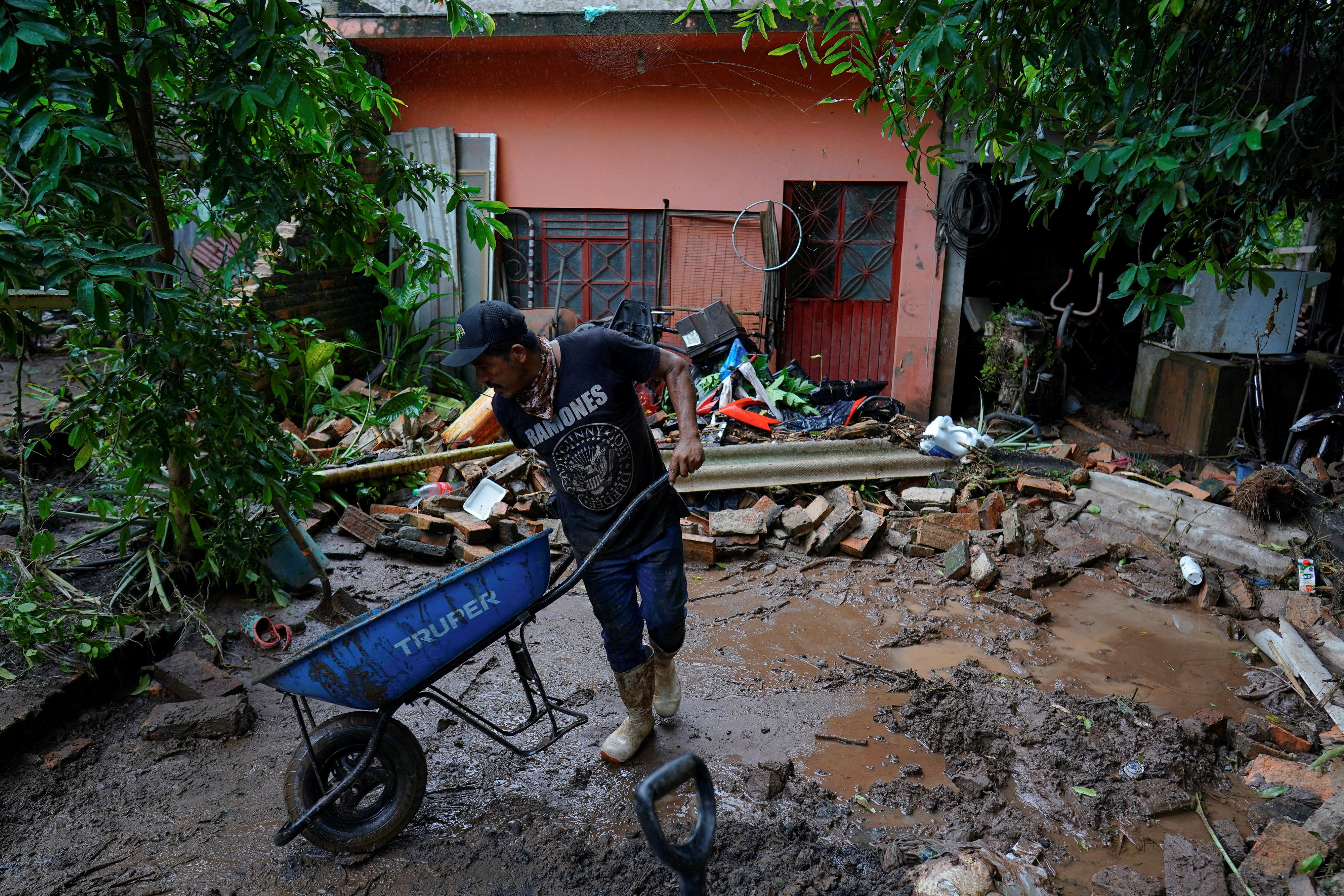 A man uses a wheelbarrow to remove mud and debris from a home as torrential rains from tropical storm Raymond