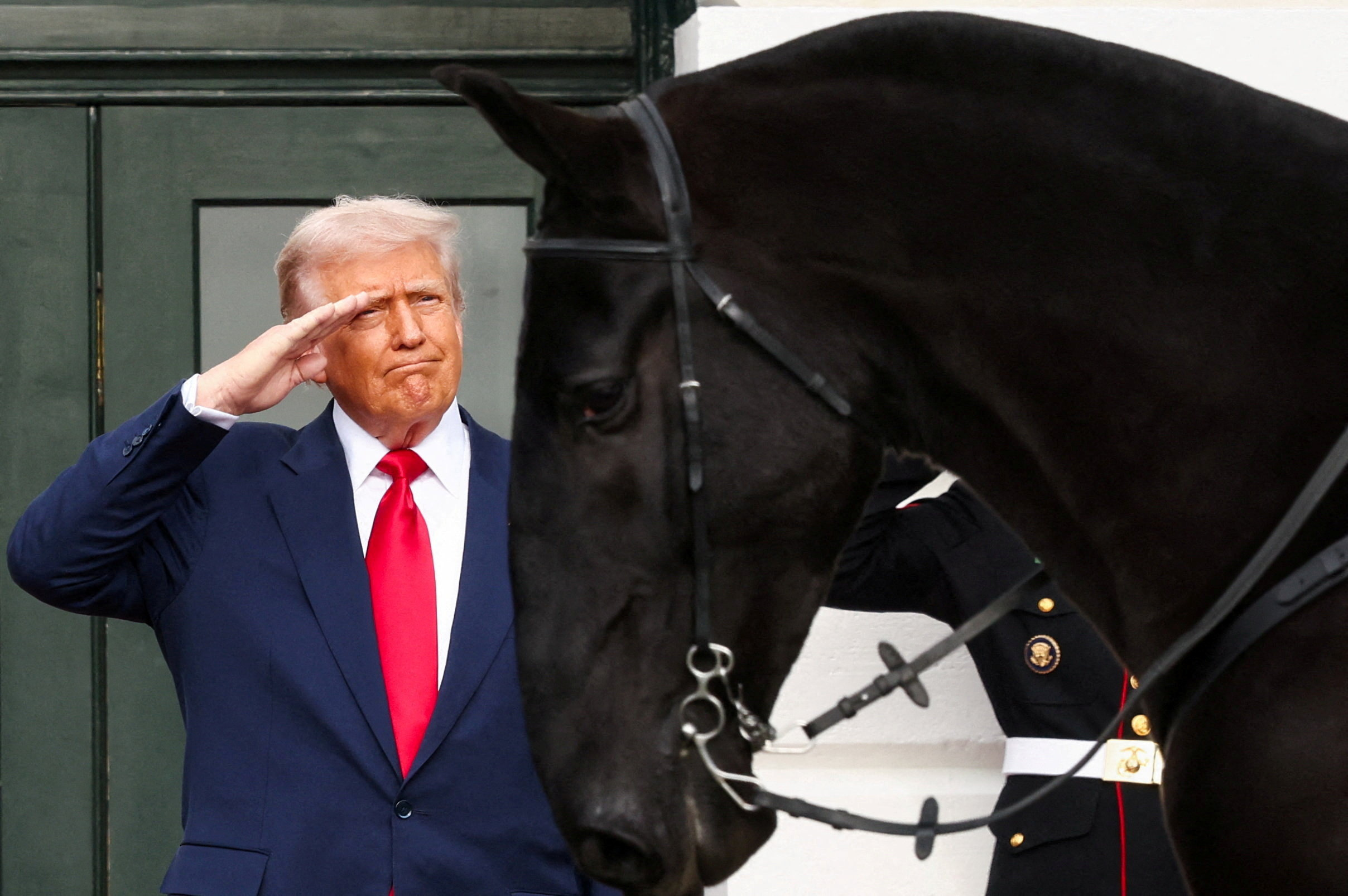 U.S. President Donald Trump salutes, as he observes a procession of horses passing the White House ahead of the arrival of Saudi Crown Prince and Prime Minister Mohammed bin Salman, in Washington, D.C., U.S., November 18, 2025. REUTERS/Kevin Lamarque