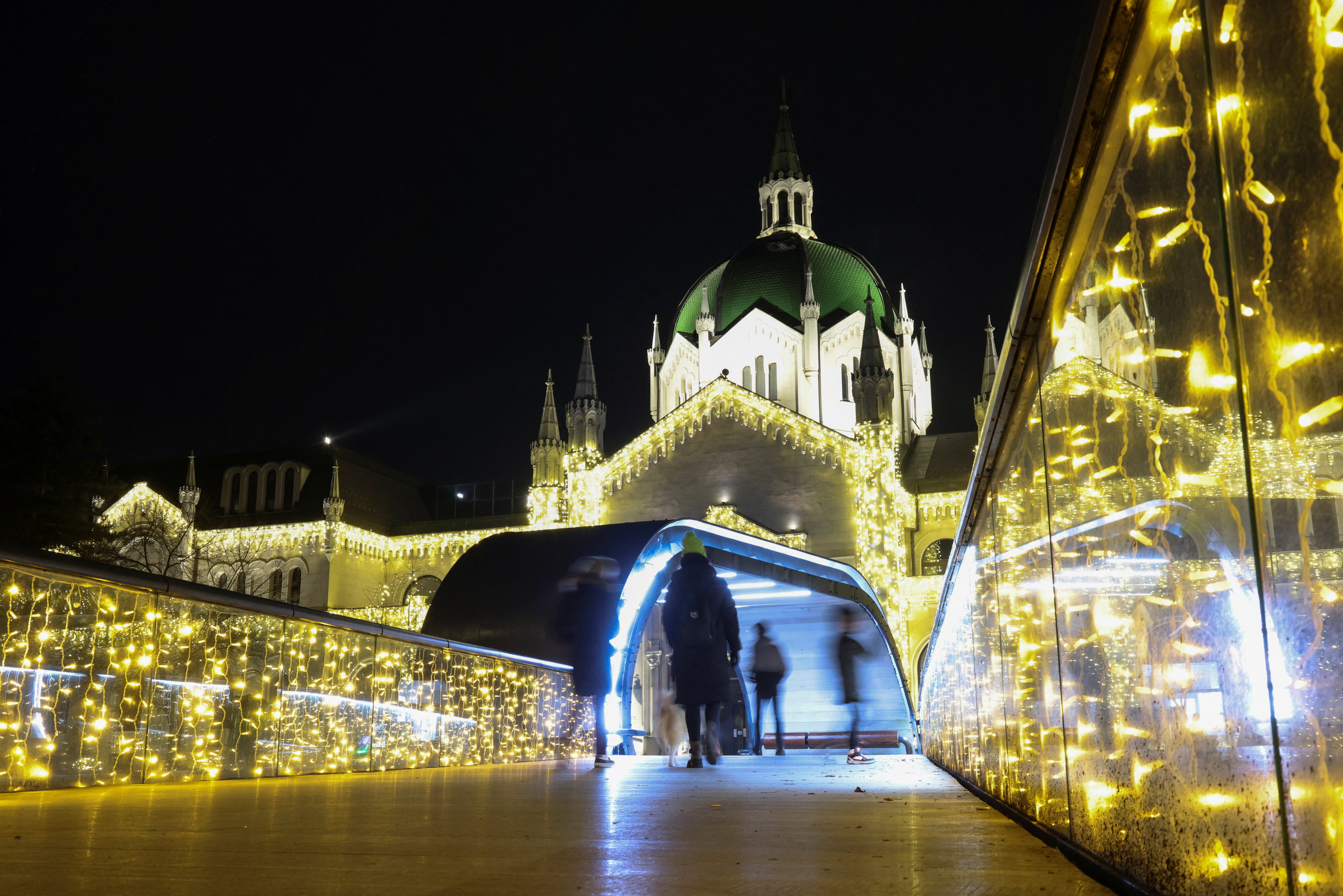 People walk on a bridge near the Academy of Fine Arts decorated with lights for upcoming holidays in Sarajevo, Bosnia and Herzegovina, December 21, 2025. REUTERS/Amel Emric