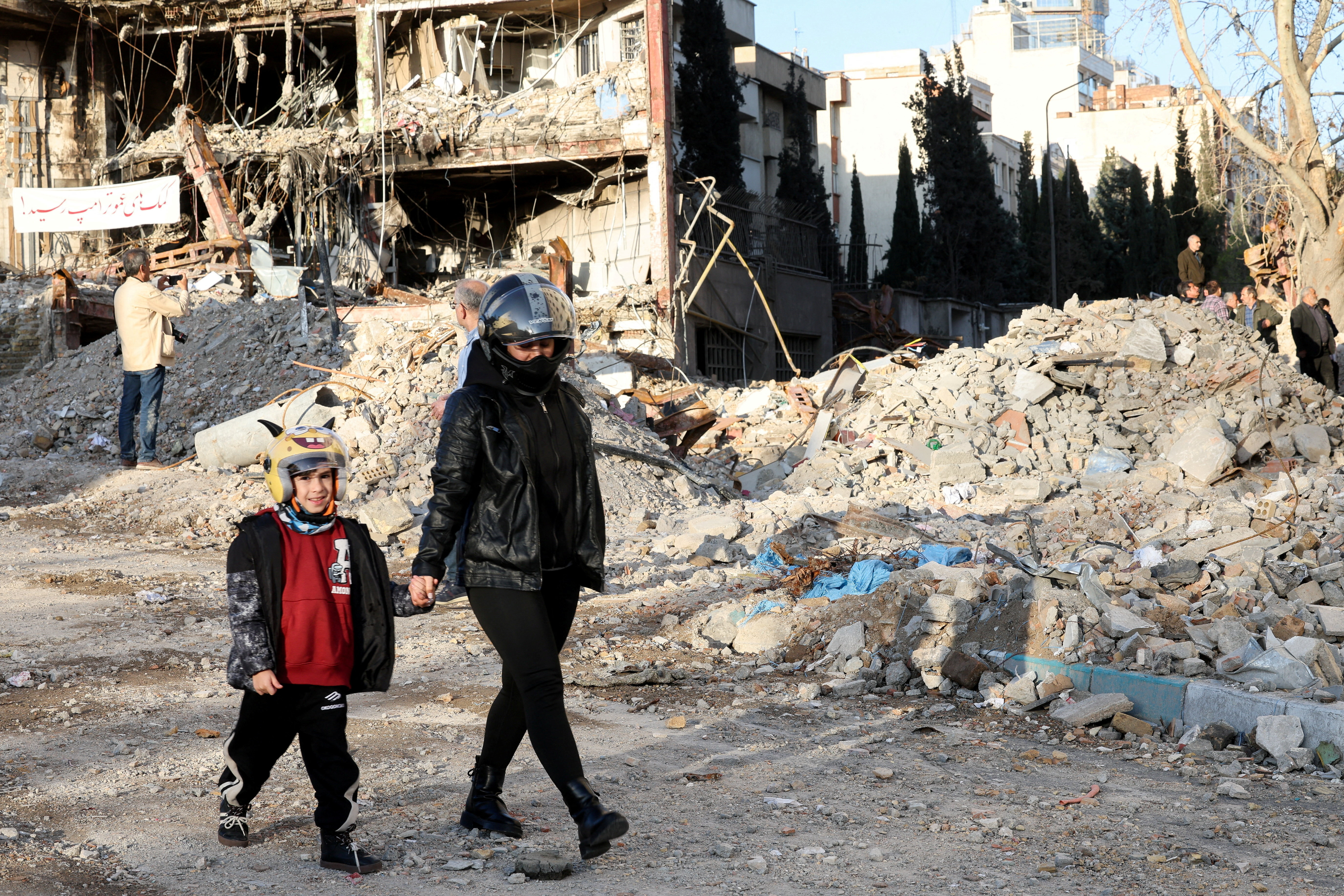 A mother and son walk near a building destroyed in a strike, amid the U.S.-Israeli conflict with Iran, in Tehran, Iran, March 21, 2026. Reuters/Alaa Al-Marjani