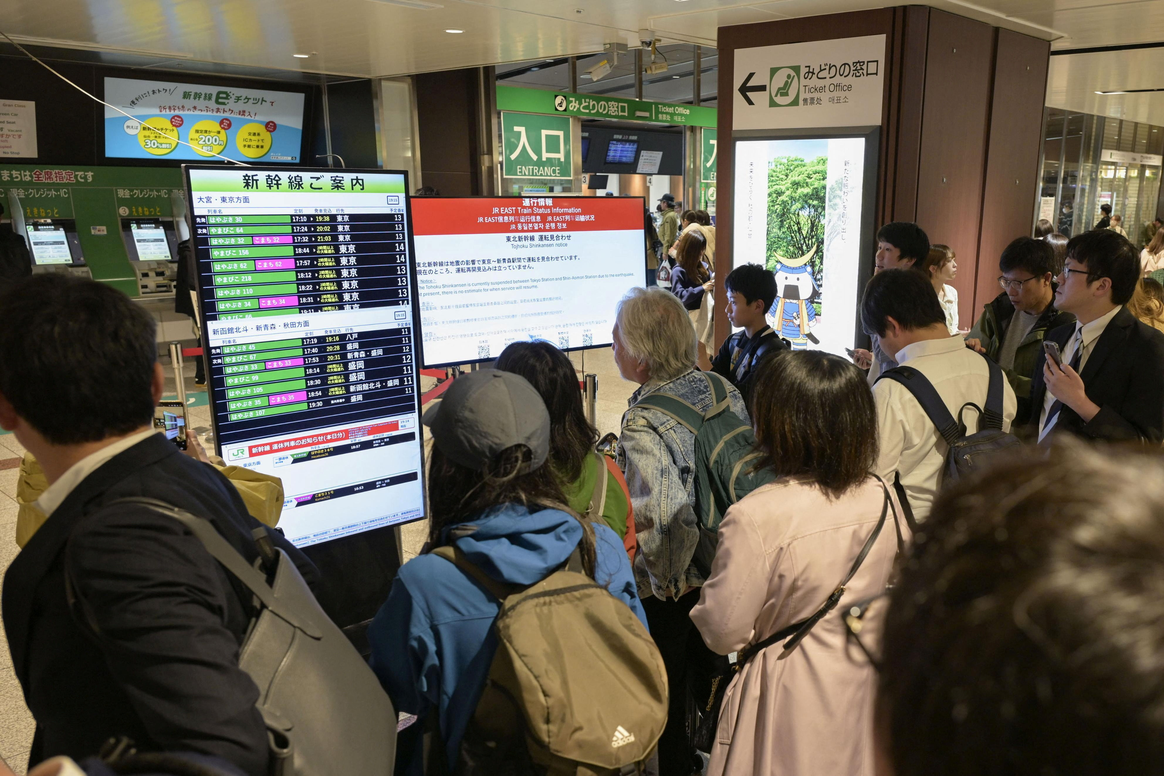 Passengers look at electronic screens announci