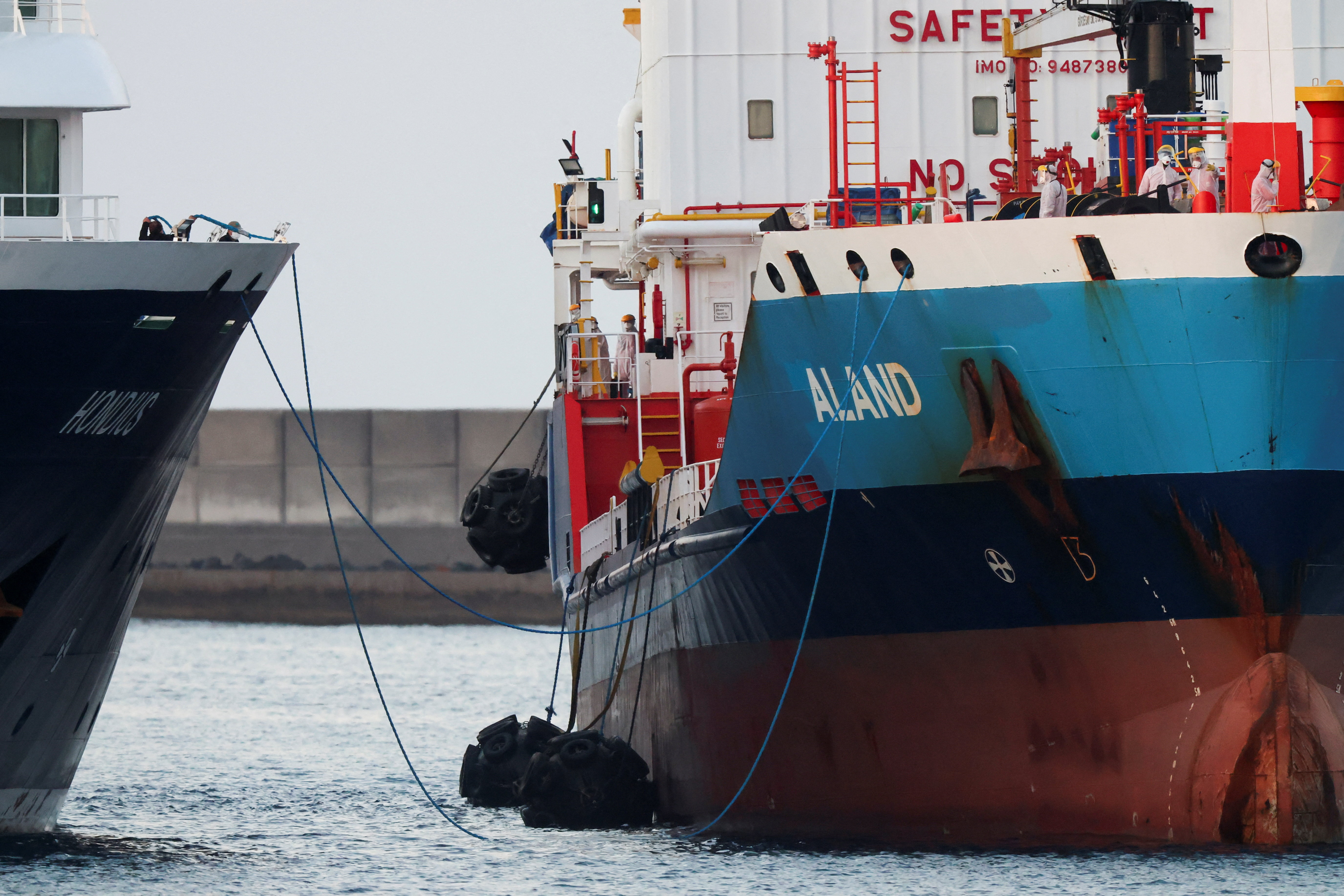 Workers in personal protective equipment (PPE) stand aboard a tanker next to the cruise ship MV Hondius,  affected by a hantavirus outbreak, at the port of Granadilla de Abona, in Tenerife, Spain, May 11, 2026. REUTERS/Hannah McKay