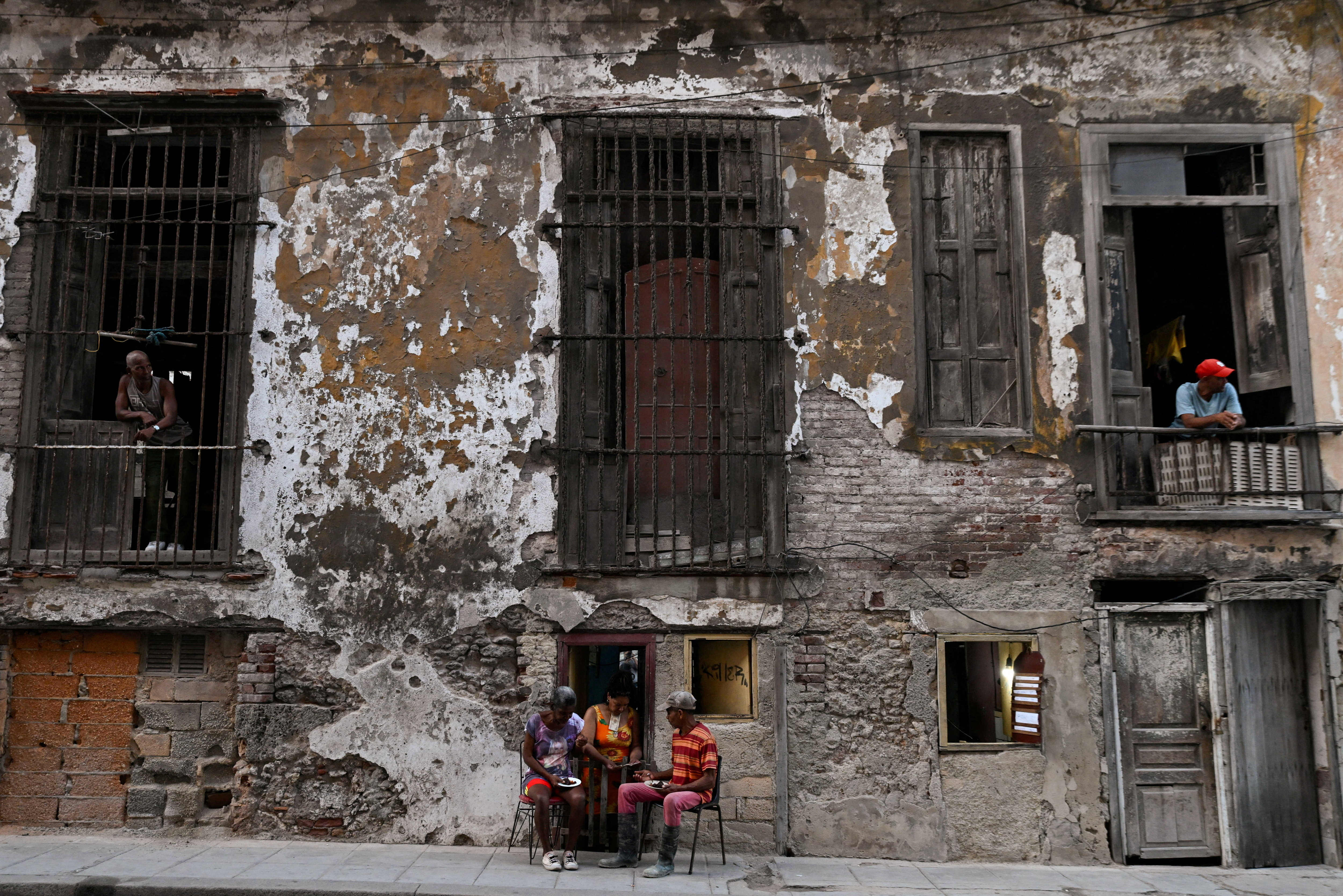 People eat outside of a small cafeteria while neighbors look out from a balcony