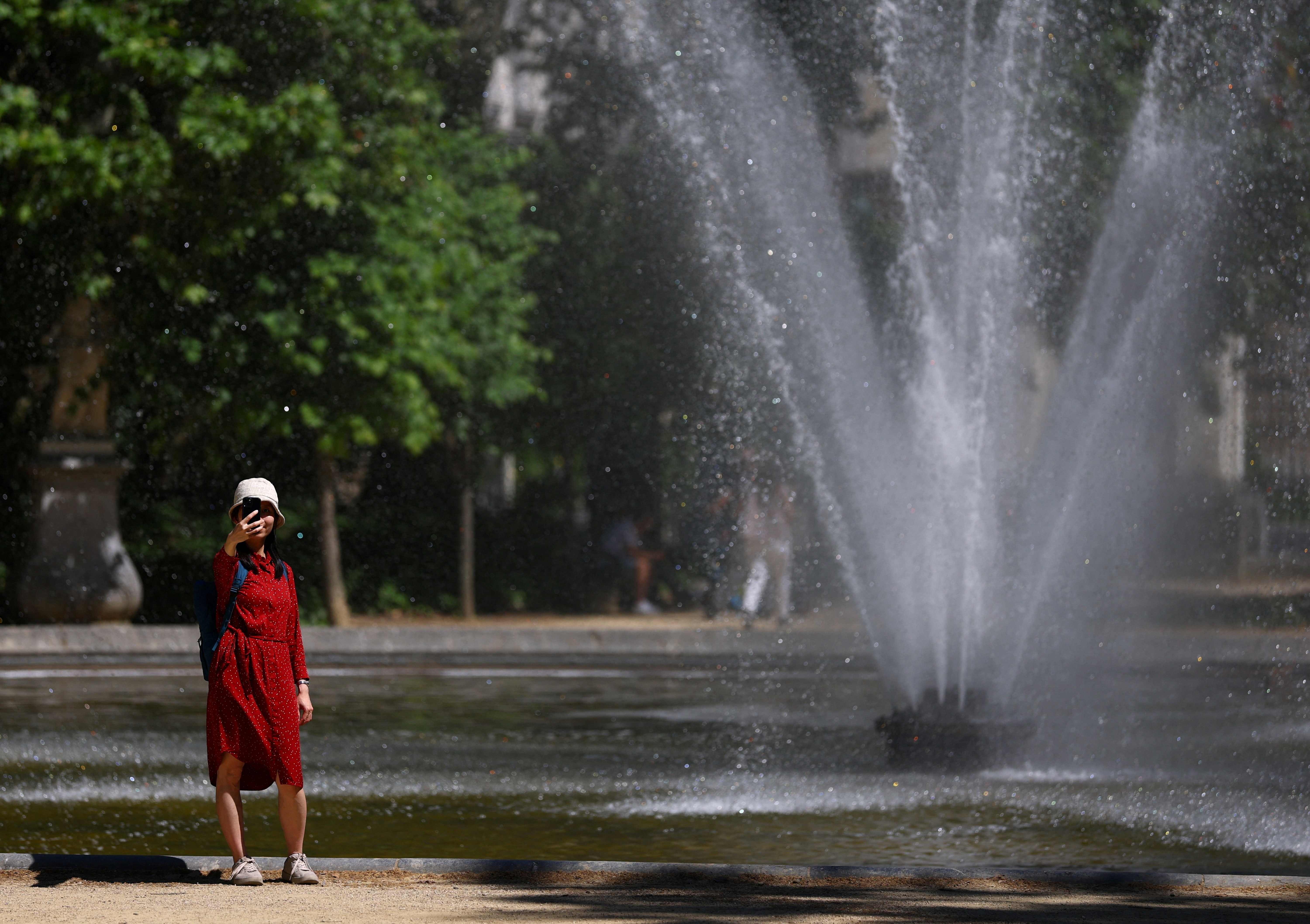 A person stands near a fountain in a park as the heat wave grips Europe, in Brussels, Belgium June 18, 2026. REUTERS/Yves Herman