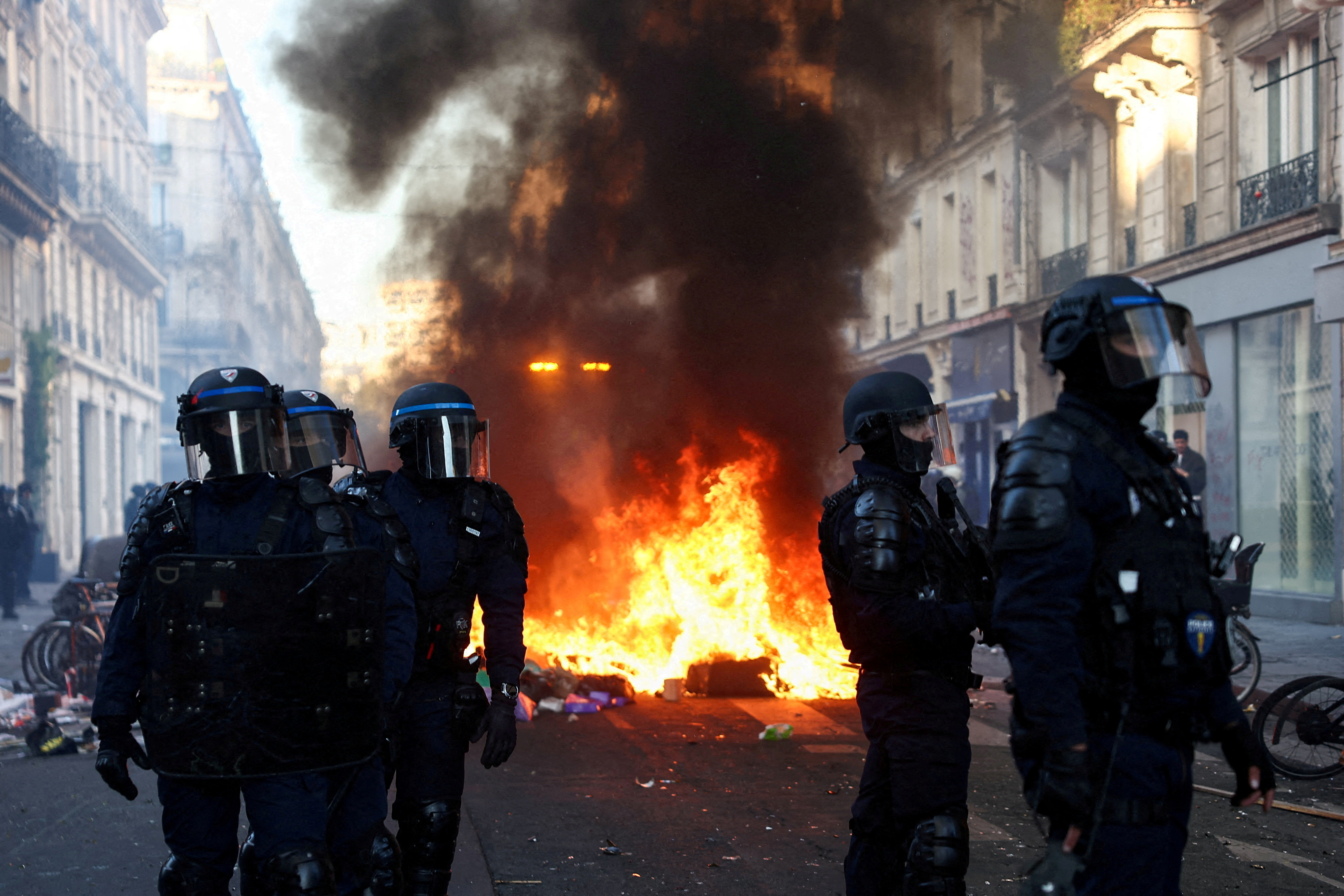 A fire burns, as Police officers in riot gear stand guard, during civil unrest, the day after a national day of demonstrations against the cost of living and rising fuel prices, in Paris