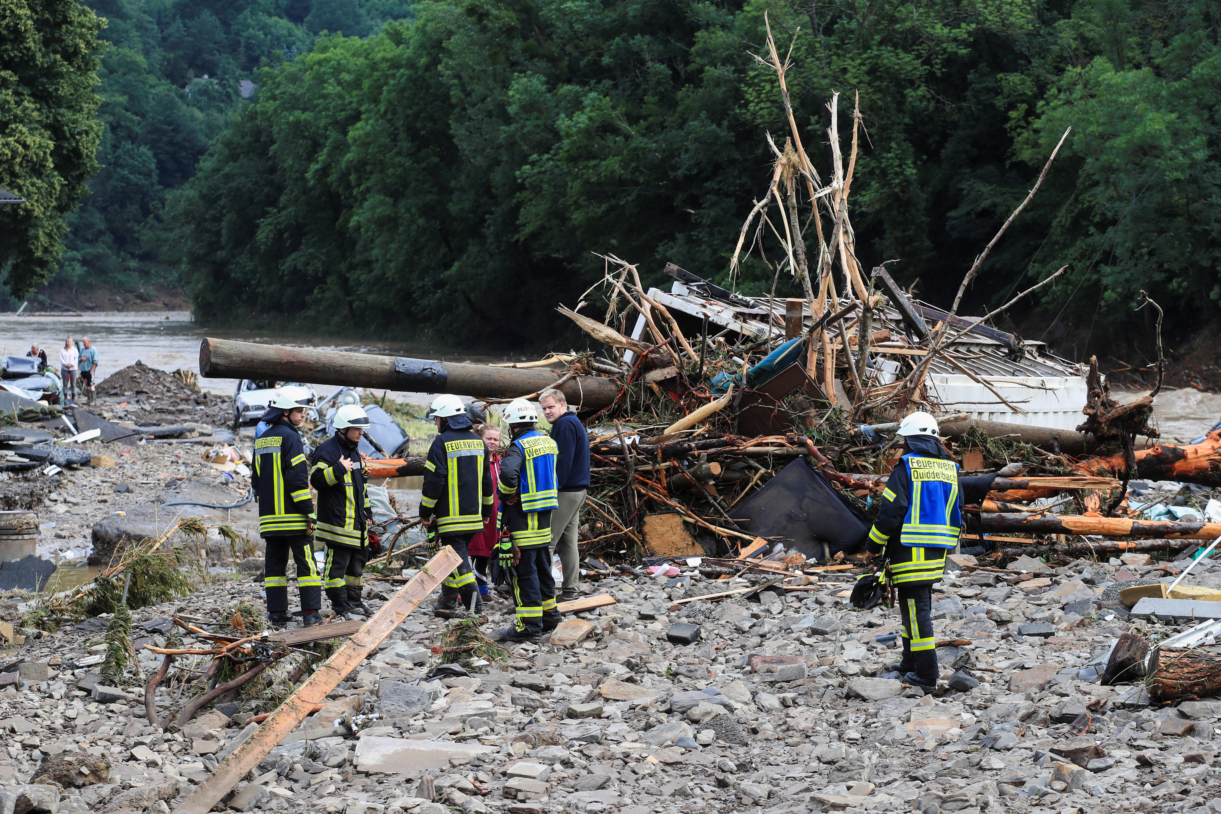 Firefighters speak with people next to debris brought by the flood following heavy rainfalls in Schuld