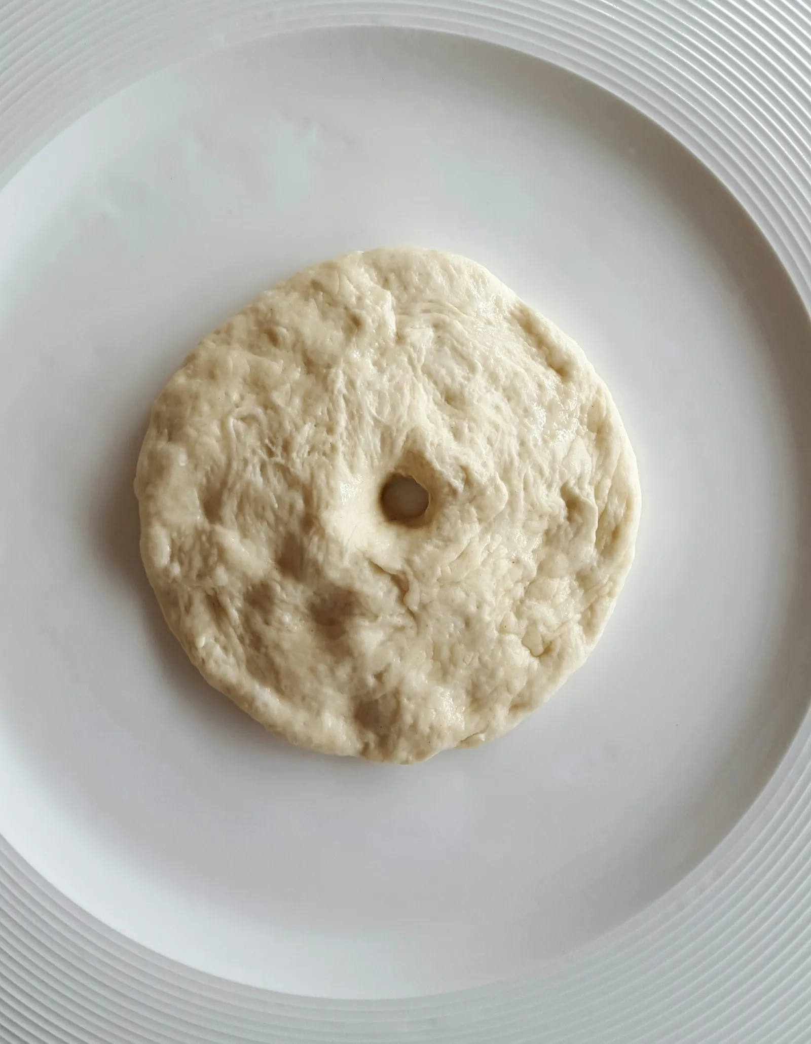 A round piece of raw dough with a hole in the center, placed on a white plate.