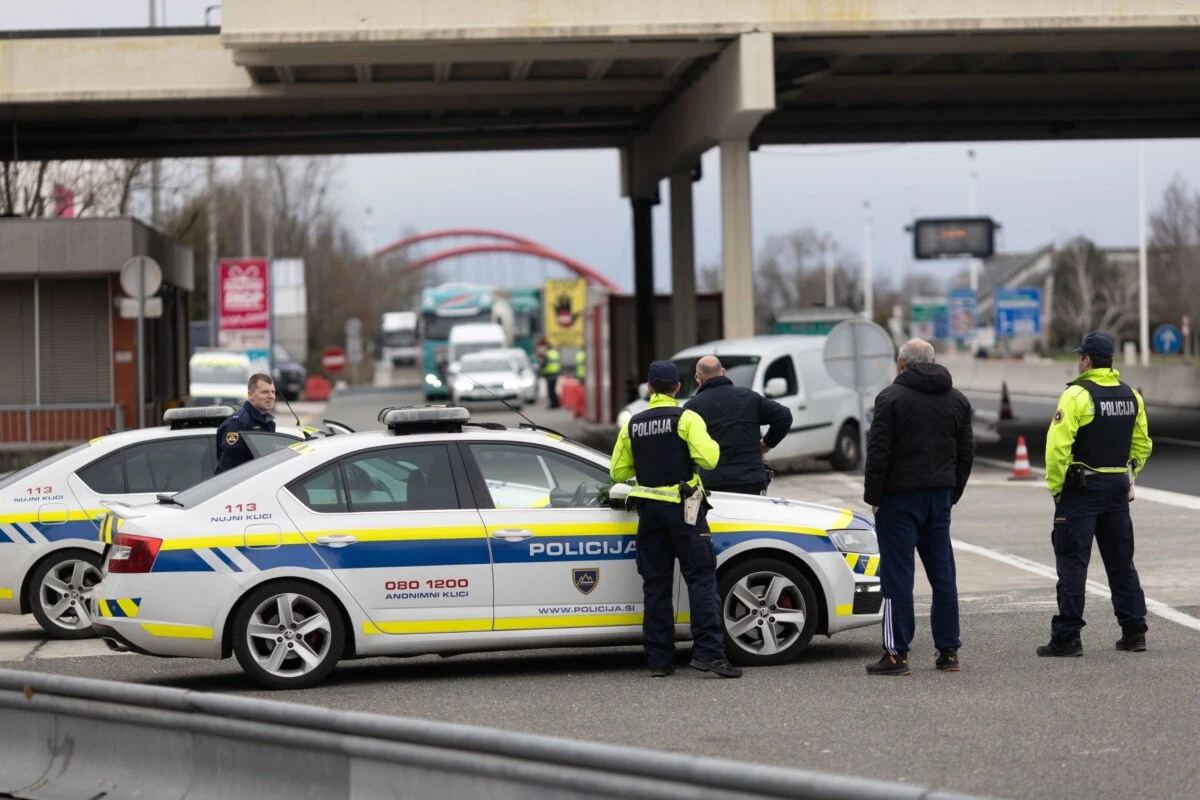 Police officers and patrol cars in Slovenia at a checkpoint, with a bridge visible in the background.