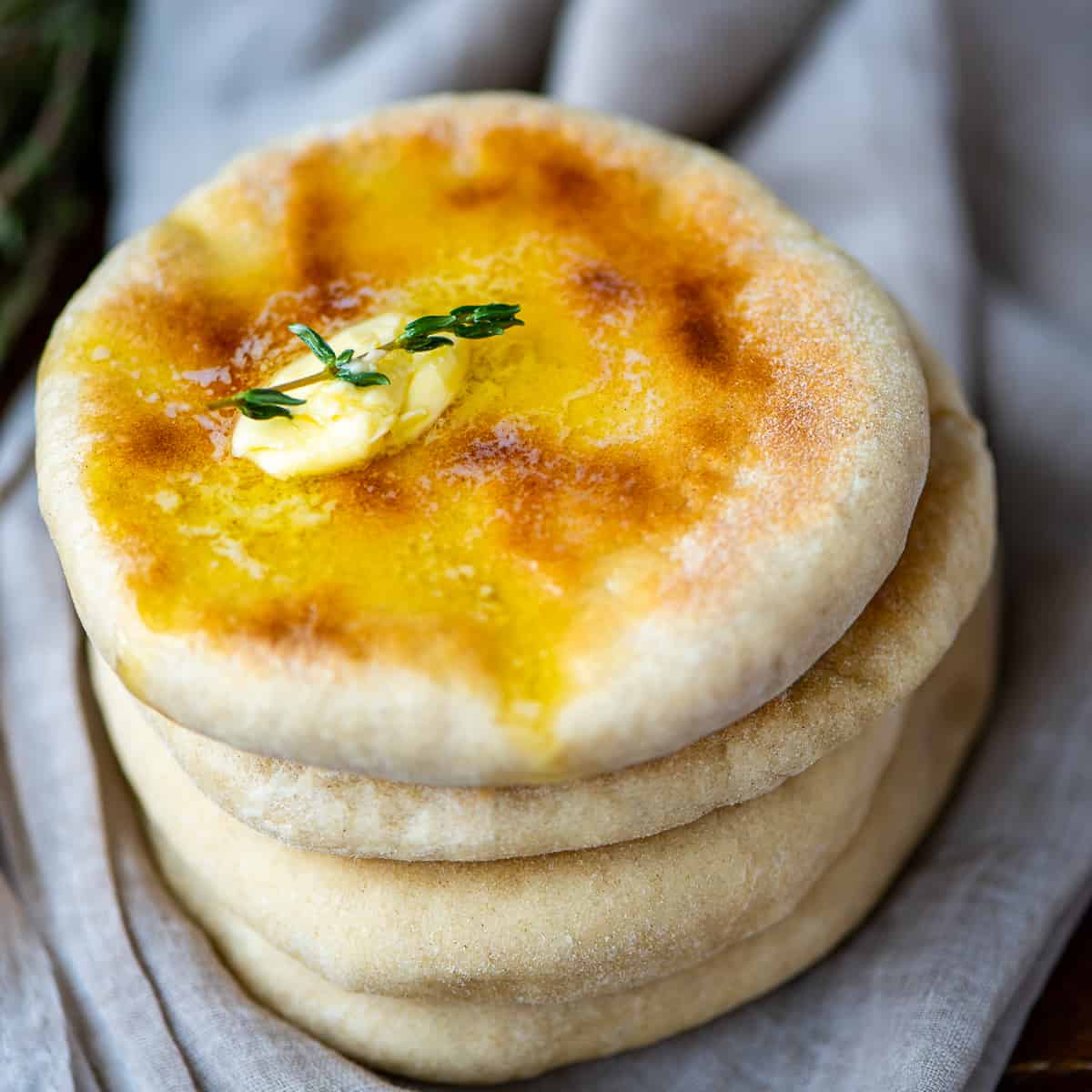 A stack of freshly baked bazlama, a type of Turkish flatbread, topped with melted butter and herbs.
