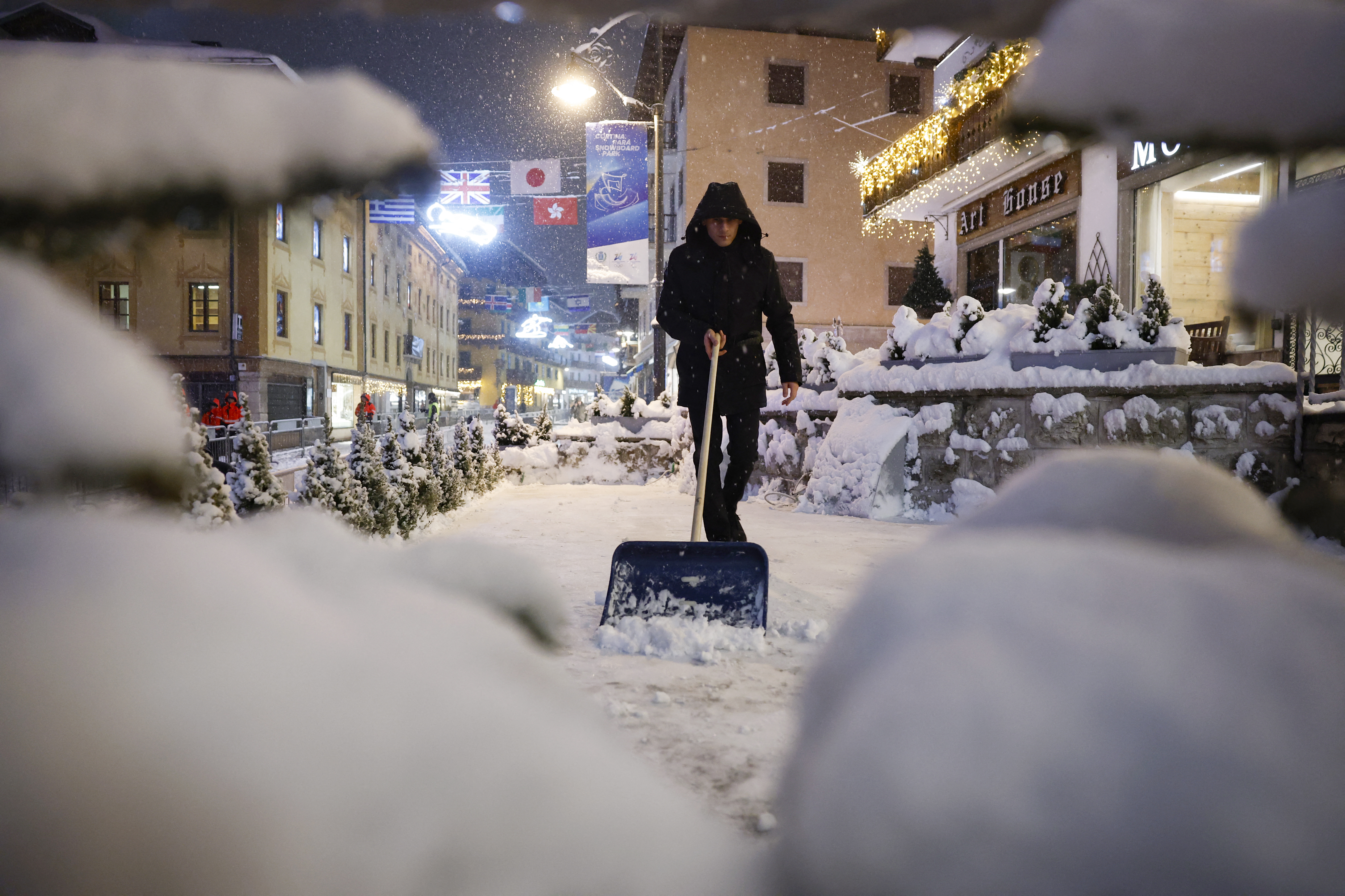 A business manager shovels snow outside a restaurant during snowfall in the main shopping area in Cortina d'Ampezzo on February 4, 2026, ahead of the Milano Cortina 2026 Winter Olympic Games. (Photo by Odd ANDERSEN / AFP)