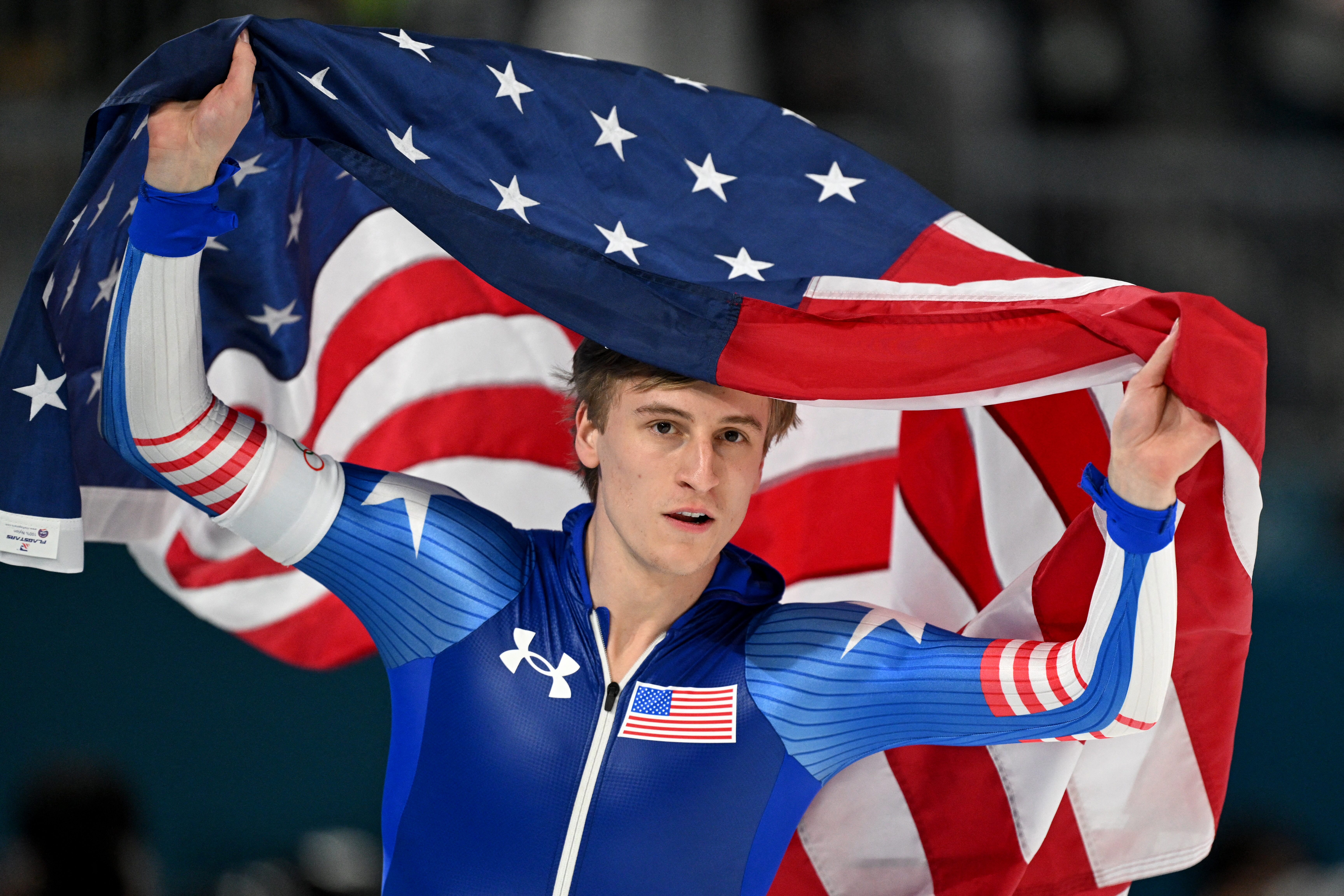 USA's Jordan Stolz holds his country's flag after winning gold in the speed skating men's 500m during the Milano Cortina 2026 Winter Olympic Games at Milano Speed Skating Stadium in Milan on February 14, 2026. (Photo by Daniel MUNOZ / AFP)