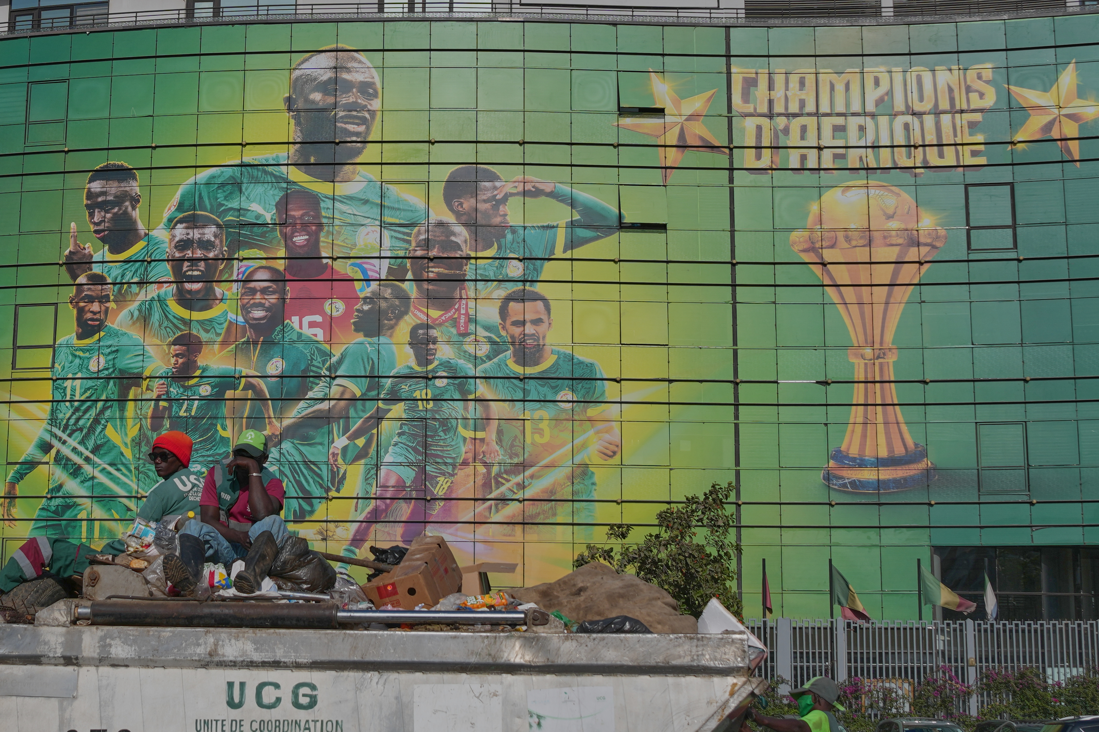 People sit on top of a car as they pass by a mural celebrating Senegal's victory in the Africa Cup of Nations, which covers a building in Dakar, Senegal, Wednesday, March 18, 2026. (AP Photo/Misper Apawu)