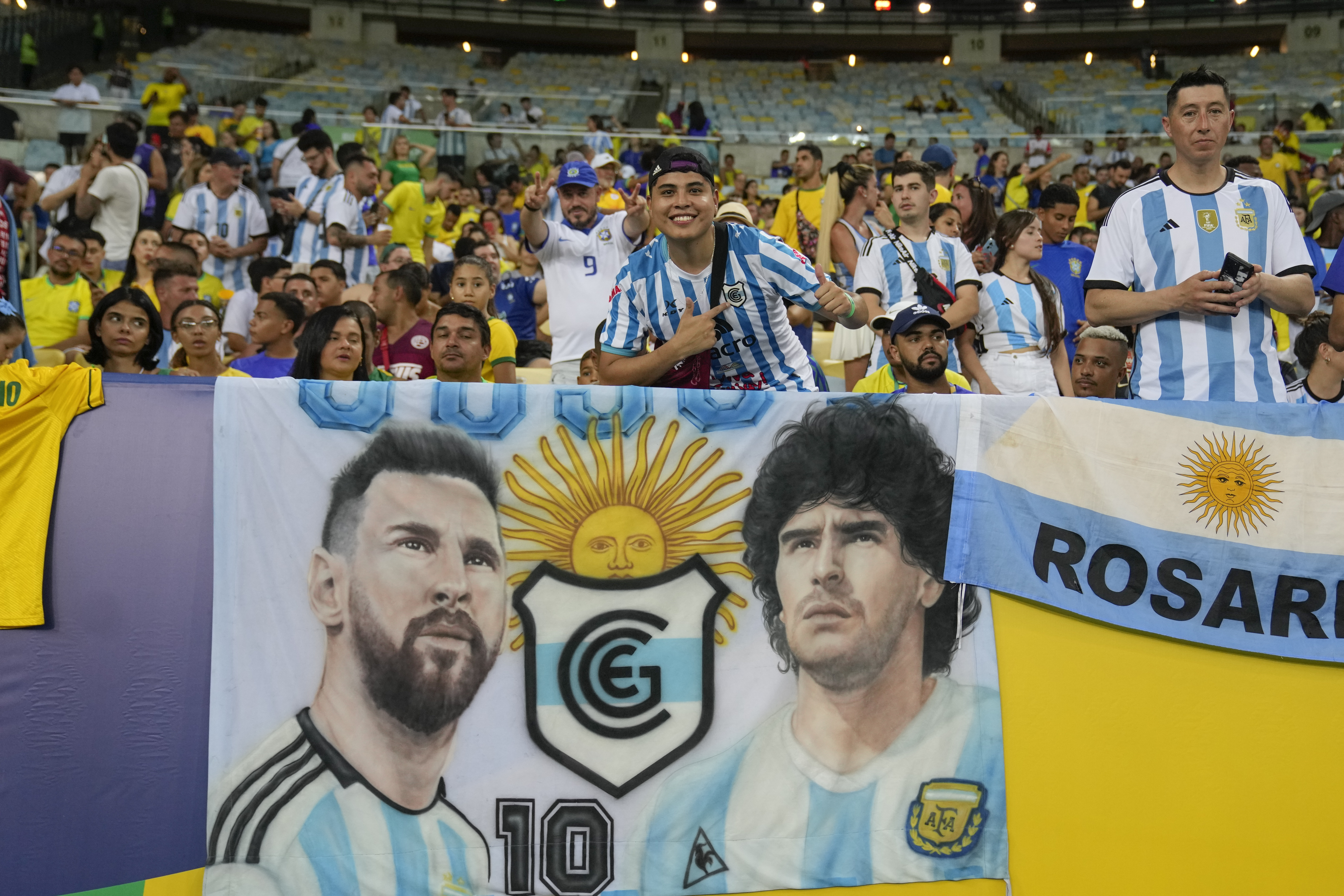 Fans cheer next to a banner featuring Argentina's Lionel Messi and late soccer great Diego Maradona prior to the start of a qualifying soccer match for the FIFA World Cup 2026 against Brazil at Maracana stadium in Rio de Janeiro, Brazil, Tuesday, Nov. 21,