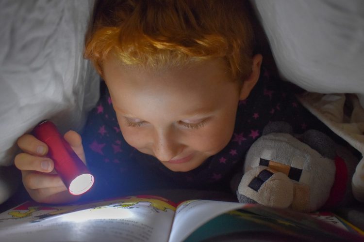 Dijete čita ispod jorgana sa baterijskom lampom