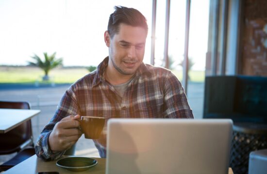 nasmijeseni muskarac koristi laptop dok pije kafu