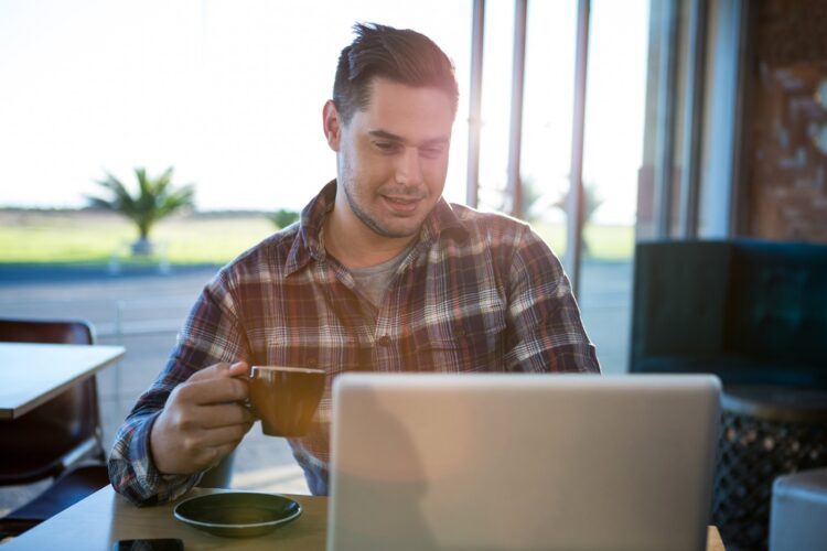 nasmijeseni muskarac koristi laptop dok pije kafu